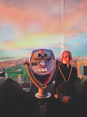 Girl looking through a telescope at the NYC skyline at sunset