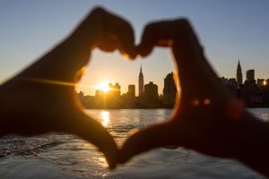Hands making a heart with the New York City skyline in the background