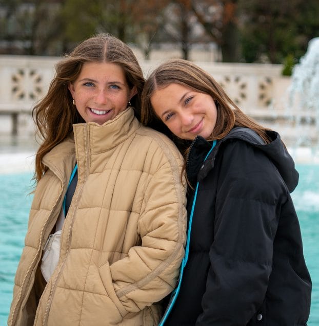 Two students smiling together in front of a fountain.
